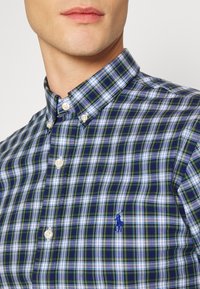 Košile s kostkovaným vzorem v zelené, modré a bílé barvě s knoflíky. Obsahuje bílé knoflíky a malé modré logo na hrudi. Bavlněná tkanina.