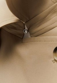 Gros plan sur un tissu beige avec des coutures cousues, une boutonnière et un anneau métallique fixé à l'intérieur d'une section pliée.