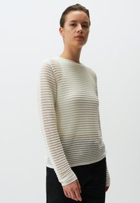 Pull en tricot blanc avec un design à rayures texturées, doté de manches longues et d'un col rond. Matériau léger et respirant.