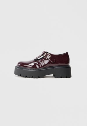 Burgundy patent leather Mary Jane shoe with silver buckle and chunky black lug sole, side view on white background.