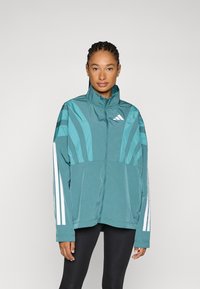 Tirkizna jakna na patent s visokim ovratnikom, vertikalne pruge na ramenima i bijele Adidas pruge na rukavima. Lagana, teksturirana tkanina.