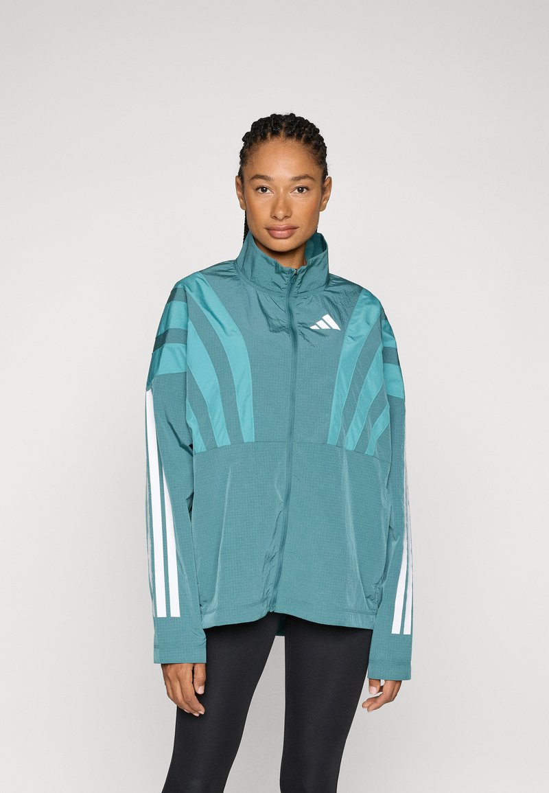 Tirkizna jakna na patent s visokim ovratnikom, vertikalne pruge na ramenima i bijele Adidas pruge na rukavima. Lagana, teksturirana tkanina.