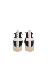 Baskets montantes noir et blanc avec une surface texturée, des sangles blanches contrastantes, des accents rouges et une semelle beige avec des détails rayés.