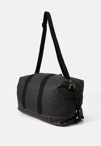 Black duffel bag with long adjustable shoulder strap and plaid fabric base, black handles, and gold-tone hardware on a white background.