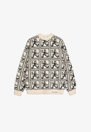 Pull en tricot beige avec un motif géométrique et figuratif noir répétitif, col rond côtelé et manches longues. Détails de texte au niveau de l'ourlet.