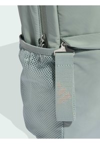 Mochila verde claro fabricada con tela suave. Cuenta con un bolsillo lateral de malla, cierres de cremallera y una correa texturizada con detalle del logo.