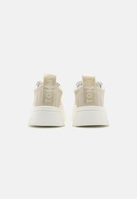 Beżowe sneakersy z teksturowaną cholewką, posiadające białą, grubą podeszwę oraz uchwyt z napisem "TOMMY" z tyłu.