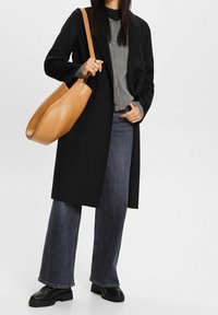 Černý dvouřadý kabát přes šedý žebrovaný svetr, doplněný o tmavé džíny s vysok�ým pasem a černé platformové boty, s tan koženou taškou.