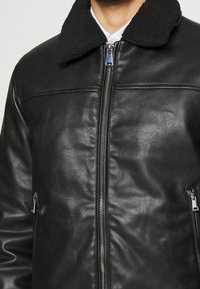 Czarna skórzana kurtka z miękkim, czarnym kołnierzem z baranka, zamkiem błyskawicznym z przodu i dwoma bocznymi kieszeniami na zamek. Teksturowana powierzchnia z poziomym przeszyciem.