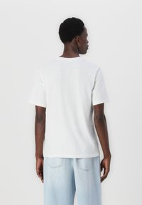 Camiseta de algodón blanca con mangas cortas, cuello redondo clásico, ajuste relajado y textura lisa. Combinada con pantalones de mezclilla azul claro.
