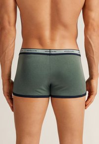 Gröna bomullsboxershorts med ett marinblått midjeband som har varumärket "intimissimi" i ett upprepande mönster. Slät textur, snygg passform.