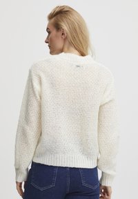 Chunky knitted sweater in off-white, featuring a ribbed hem and cuffs. It has a relaxed fit with a round neckline and a textured finish.