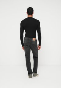 Mustast pikast varrukast top, istuva lõikega; kombineeritud tumehallide teksadega, millel on tagumine silt. Modell kannab heledaid halli värvi tossusid.