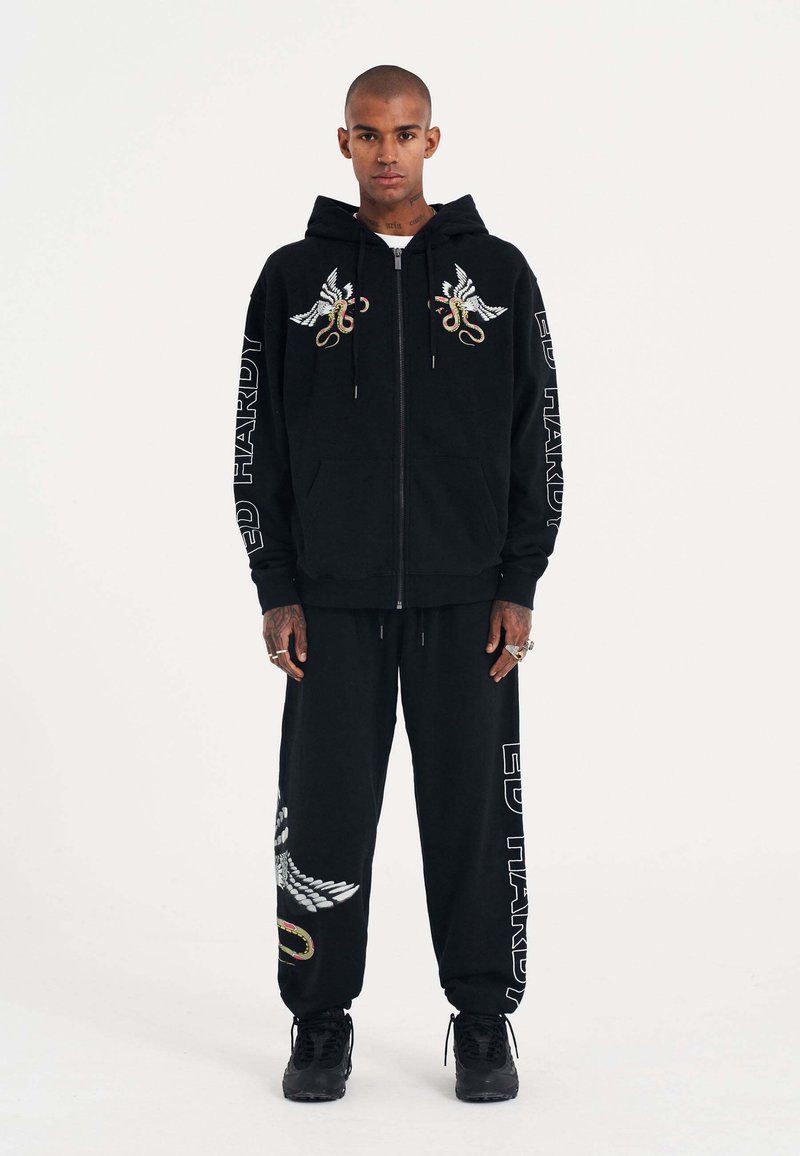 Schwarze Zip-Hoodie und passende Hose, mit gestickten Flügel- und Schlangendesigns, "ED HARDY"-Text, dickem Stoff und lockerer Passform.