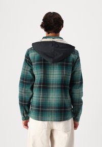 Grön och svart rutmönstrad skjorta med en grå huva, som har långa ärmar och en bekväm passform, tillverkad av textilmaterial.