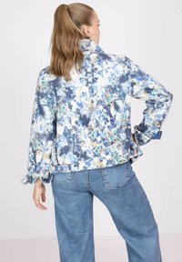 Floral-patterned, lightweight jacket in blue, white, and orange hues with a collar and gathered cuffs, paired with blue denim pants.