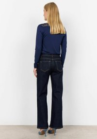 Marinbl�å långärmad topp med spetsdetalj på baksidan, ihopparad med mörkblå högmidjade raka jeans och ljusblå klackskor.