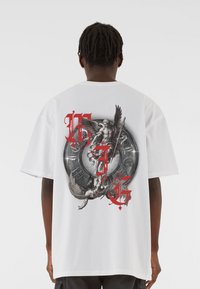 Biela oversized tričko s detailným grafickým potlačou v čiernej a červenej farbe, zobrazením mytologických postáv a kruhových prvkov.