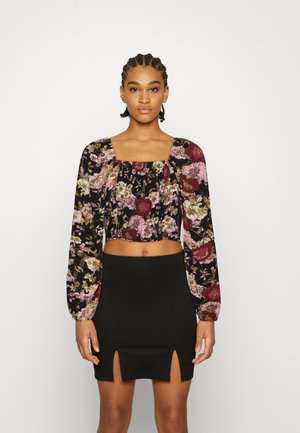 Top cropped preto com padrão floral apresentando tons de bordô, rosa e verde. Combinado com uma saia preta justa com fendas laterais.