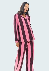 Pajama set s pruhy ve širokých růžových a tmavě hnědých pruzích, vyrobený z měkké tkaniny, zahrnuje košili na knoflíky a odpovídající kalhoty.