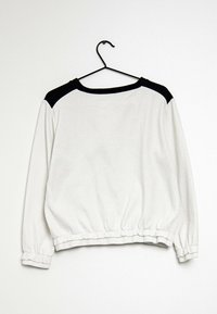 Sudadera blanca con acentos negros en los hombros, cuello redondo y dobladillo y puños elásticos fruncidos. Tela suave con un diseño casual.