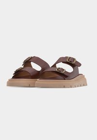 Sandales en cuir marron avec deux boucles en laiton réglables sur des semelles épaisses beige aux bords rainurés sur fond blanc.