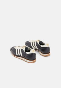 Navy blue athletic shoes with three white stripes, cream accents, and a rubber sole. Features a textured finish and classic lace-up design.