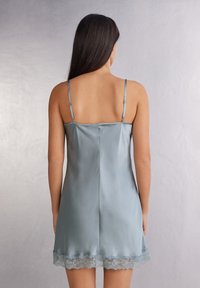 Jedwabna, jasnoniebieska sukienka na ramiączkach z cienkimi paskami i koronkowym wykończeniem u dołu. Gładka faktura, prosty krój oraz detal szwu w tylnej części.