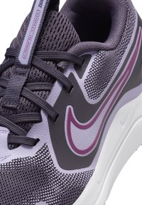 Gros plan sur une chaussure de course Nike violet et gris avec une tige en mesh, un laçage à l'avant et une semelle blanche, arborant un logo swoosh bordé de rose.