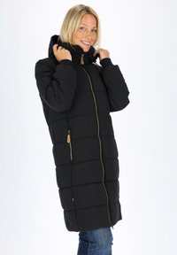 Piumino nero con una silhouette lunga, design a righe verticali, chiusura frontale con zip e cappuccio regolabile. Accentatura in oro sulla zip e tasche laterali.