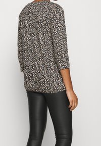 Bluse mit Blumenmuster und Dreiviertelärmeln, schwarzer Hintergrund, mit weißen und roten Blumen, kombiniert mit schwarzen Lederleggings.