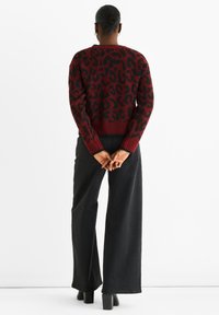 Red and black leopard print sweater with a ribbed hem and cuffs, worn with wide-leg black trousers and heeled boots. Rear view.