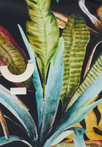 Kankaan kukkakuosi, jossa on kirkkaan vihreitä ja keltaisia lehtiä mustalla taustalla, ja vaaleat kirjaimet integroituina suunnitteluun.