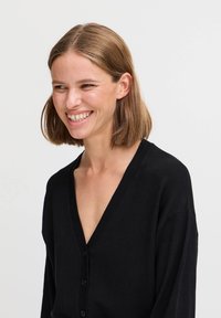 Cardigan nero con scollatura a V profonda, maniche lunghe, bottoni frontali e una superficie liscia. Design semplice senza motivi o dettagli visibili.