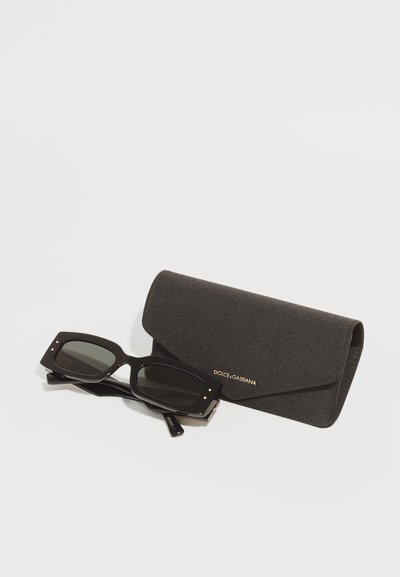 Dolce & Gabbana melnas saulesbrilles ar kvadrātveida rāmjiem un pelēkiem stikliem, pievienotas melnai teksturētai maciņai ar zelta logo.