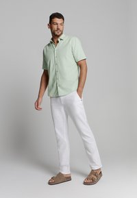 Lichtgroene kortegym-button-up shirt, witte broek en bruine sandalen. Het shirt heeft een casual pasvorm en een zachte stoftextuur.