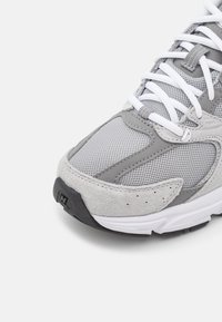 Šedá sportovní bota s kombinací síťoviny a semiše, výrazné bílé šňůrky a texturovaná gumová podrážka se znakem.