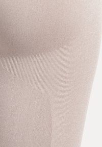 Beige compressiebroek met een gladde textuur en geribbelde delen. De stof vertoont een subtiele glans en verschillende patronen in de weving.