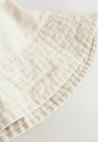 Chapeau seau en coton beige clair avec une texture matelassée et un large bord arrondi. Détails de couture visibles le long du bord.
