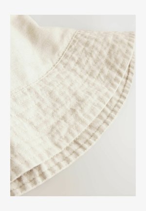 Helebeige puuvillane ämbri müts, millel on tikanditöödega tekstuur ja lai, ümar ääreosa. Serva ääres on nähtavad õmblustead.