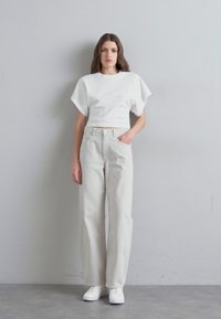 T-shirt blanc court avec des manches larges, associé à un pantalon droit taille haute de couleur gris clair. Le modèle porte des baskets blanches.