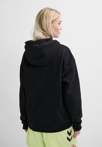 Svart huva tröja i bomullsblandning med avslappnad passform, ribbad mudd och känguruficka. Bärs med ljusgröna shorts.