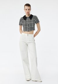 Zwart-wit geruite, kortere shirt met kanten kraag; gecombineerd met hooggewaisted, wijde witte broek; gladde stof en getailleerde stijl.