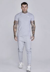 Grey short-sleeve t-shirt and matching joggers made of soft fabric, featuring elastic waistband and embroidered logo on the chest and thigh.