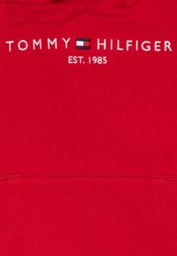 Felpa rossa con ricamo del testo "TOMMY HILFIGER" e del logo della bandiera sopra "EST. 1985". Tessuto liscio con dettagli a coste.