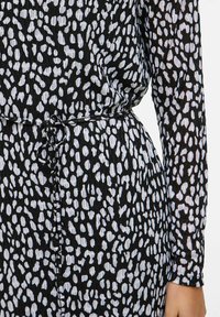 Abito nero con un motivo astratto bianco, maniche lunghe e vita con coulisse. Il tessuto ha un aspetto texture.