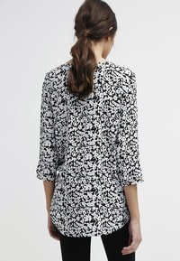 Svart och vit blus med blommönster, trekvartsärmar och avslappnad passform. Tyget verkar lätt och har en jämn textur.