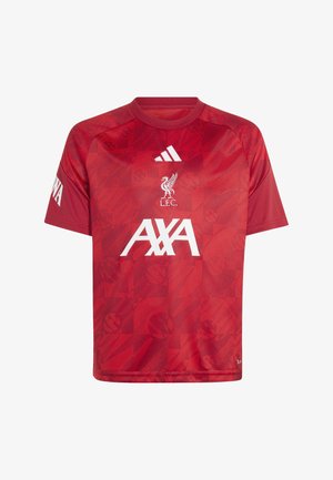 Garçon portant un maillot rouge du Liverpool FC et un pantalon noir Adidas tenant un ballon de football noir et blanc, souriant, debout sur fond blanc.