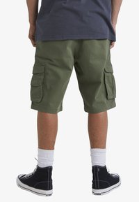 Olive green cargo shorts with multiple side pockets, a relaxed fit, and hem hitting mid-thigh. Paired with black high-top sneakers.