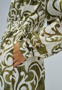 Vestido con estampado verde y blanco, con cintura ajustada, mangas largas y un acabado texturizado. Cuenta con un bolsillo y puños abotonados.